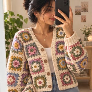 Może przedstawiać: Kardigan z długim rękawem wykonany z kremowej włóczki, ozdobiony wielokolorowym wzorem kwadratów typu granny square z motywami kwiatowymi w odcieniach różu, żółci, zieleni i błękitu. Ubiór posiada dekolt w serek i cztery brązowe guziki.