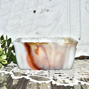May include: A white, brown, and orange swirl glass dish with a fluted rim. The dish is made of opaque glass and has a marbled pattern.