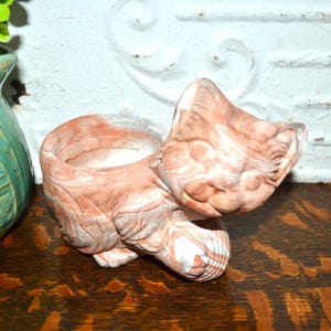 May include: A ceramic cat-shaped planter with a marbled effect in shades of brown, white, and gray. The planter has a hollowed-out center for holding small plants or decorative items. The cat is in a seated position with its head tilted.