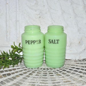 Puede incluir: Un juego de dos saleros y pimenteros vintage. Los saleros son de vidrio verde y tienen un diseño acanalado. Las palabras "SAL" y "PIMIENTA" están impresas en negro en la parte delantera de los saleros.