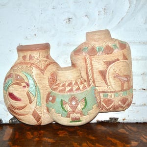 May include: Three beige ceramic vases with detailed carved patterns. The vases display geometric and animal designs in brown, red, and teal. The vases are grouped together, forming a decorative arrangement.
