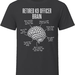 May include: A charcoal gray t-shirt featuring a white graphic of a human brain. The text reads: RETIRED K9 OFFICER BRAIN, with arrows pointing to labels: Best coworker of my career had four legs, Retired us both on the same day, Partner finally gets to be just a dog, Zero interest in office politics, Best coworker of my career still has four legs, Trusted him with my life daily, Nap on the couch, both of us.