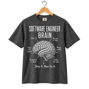 May include: A charcoal grey short-sleeve t-shirt featuring a white graphic of a human brain. The text reads: SOFTWARE ENGINEER BRAIN, Ship it, It's not a bug, Tabs not spaces, Merge conflict, Production is down, Coffee to code, Ship it, then fix it.