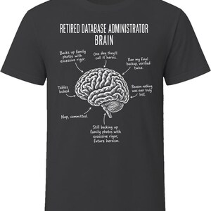 May include: A charcoal gray t-shirt featuring a white anatomical brain illustration. Text reads: RETIRED DATABASE ADMINISTRATOR BRAIN, with arrows pointing to labels: Backs up family photos with excessive rigor, One day they'll call it heroic, Ran my final backup, verified twice, Tables locked, Reason nothing was ever truly lost, Nap, committed, Still backing up family photos with excessive rigor, future heroism.