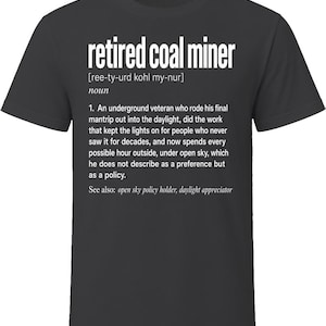 May include: A charcoal gray short-sleeved t-shirt featuring white text that defines a retired coal miner as an underground veteran who rode his final mantrip into the daylight, kept lights on for others, and now spends time under the open sky.