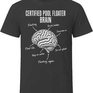 May include: A dark gray t-shirt featuring a white graphic of a human brain with arrows pointing to various parts labeled with text: CERTIFIED POOL FLOATER BRAIN, Floating, Drink holder, Sunscreen on, Float life, Nap on water, Do not splash, and Floating, again.