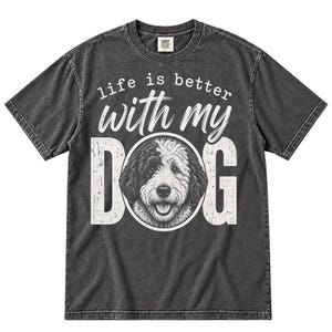 May include: A charcoal grey short-sleeve t-shirt featuring a white graphic print. The text reads "life is better with my DOG" with the letter "O" replaced by a detailed illustration of a black and white dog's face.