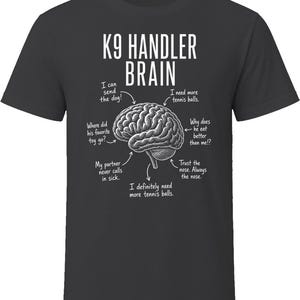 May include: A charcoal gray t-shirt featuring a white graphic of a human brain. The text reads K9 HANDLER BRAIN with arrows pointing to various thoughts including I can send the dog, I need more tennis balls, and Trust the nose. Always the nose.