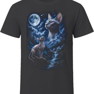 May include: A charcoal gray short-sleeve t-shirt featuring a graphic print of two hairless cats in a night landscape. One cat sits on a rock near a waterfall, while a large ethereal cat head appears in the starry sky above a full moon and mountains.