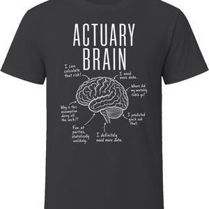 May include: A charcoal grey t-shirt featuring a white graphic of a human brain with arrows pointing to various parts. The text reads ACTUARY BRAIN, I can calculate that risk, I need more data, Where did my mortality table go, I predicted you'd ask that, I definitely need more data, Fun at parties, statistically unlikely, and Why is this assumption doing all the work!?