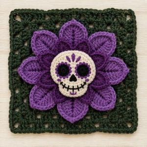 May include: A square crochet granny square featuring a dark green border and a central three-dimensional purple flower. At the center of the flower is a cream-colored skull applique with black eye sockets, a black nose, and a stitched black mouth.