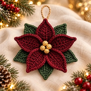 May include: A crocheted poinsettia ornament featuring deep red petals and dark green leaves. The center is adorned with four small, textured gold beads. A tan braided cord loop is attached to the top for hanging, creating a festive decoration.
