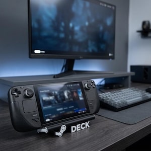 May include: A black handheld gaming console resting on a white stand that features the Steam logo and the word DECK in block letters. The console has a central screen, dual analogue sticks, a directional pad, and various buttons on its front face.