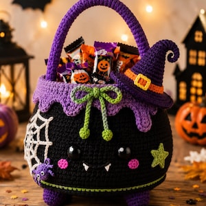 May include: A black crochet cauldron basket with a purple handle, featuring a small purple witch hat, a white spider web with a purple spider, a green star, and a green bow. The cauldron has black eyes, pink cheeks, and two white fangs.