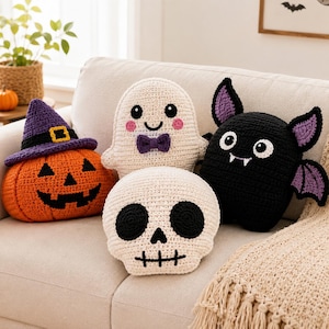 May include: Four crocheted plush pillows featuring Halloween themes: an orange pumpkin wearing a purple witch hat, a white ghost with a purple bow tie, a white skull with black eye sockets, and a black bat with purple inner wings and white fangs.