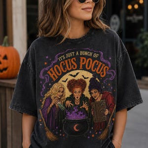 May include: A black acid-wash t-shirt featuring a graphic print of three witches around a cauldron with the text "IT'S JUST A BUNCH OF HOCUS POCUS" in orange and purple. The design includes bats, stars, and a crescent moon against a yellow circle.
