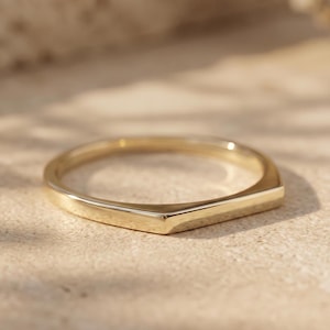 Op de afbeelding: Een gepolijste gouden ring met een V-vormig chevronontwerp. De band heeft een glad, reflecterend oppervlak met een puntig detail in het midden dat een opvallend hoekig silhouet creëert. Het metaal heeft overal een warme, gele tint.