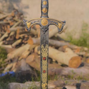 May include: A decorative sword featuring a dark metal blade with intricate gold-coloured filigree and two small red cross symbols. The hilt includes a circular pommel with a cross design, a textured grip with gold accents, and a curved crossguard.