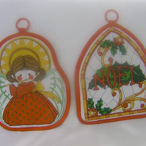 May include: Two vintage Christmas-themed pot holders. One features an angel playing a flute, wearing an orange dress with green polka dots. The other has a stained-glass design with the word "NOEL" and holly.