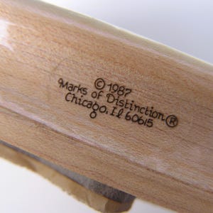 May include: Close-up of a wooden object with visible grain. The text "Marks of Distinction &copy; 1987 Chicago, IL 60615" is etched into the wood. The object appears to be a part of a larger wooden item.