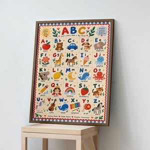 May include: A framed educational alphabet poster featuring letters A to Z in a grid format. Each letter is paired with a colourful illustration and corresponding word, such as apple, bear, car, and zebra, set against a cream background.