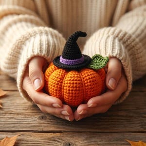 Peut inclure: Une petite citrouille crochetée orange et ronde, surmontée d'un chapeau de sorcière noir avec une bande violette et une feuille verte crochetée. La citrouille est réalisée avec des points de fil visibles et présente une surface texturée.