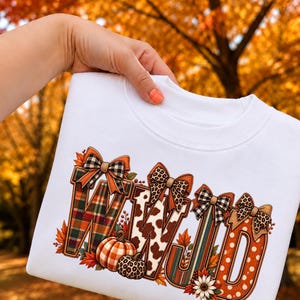 Peut inclure: Un sweat-shirt blanc à col rond arborant les lettres WWJD dans une grande police décorative. Chaque lettre est remplie de motifs variés comme du tartan, des taches de vache et des rayures, surmontée de nœuds. Des éléments d'automne sont présents.