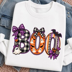 Peut inclure: Un sweat-shirt blanc à col rond avec le mot BOO en grandes lettres. Le B est à carreaux noirs et blancs avec un nœud violet et un fantôme. Le O est orange avec des fantômes blancs et un nœud. Le dernier O a des rayures orange et violettes avec une chauve-souris.