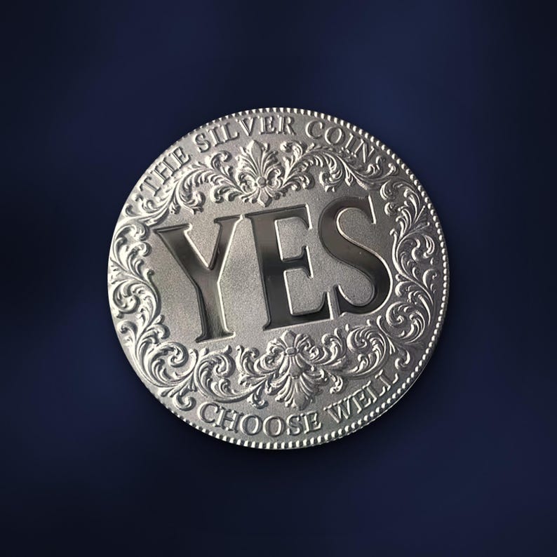 May include: A circular silver-coloured coin featuring the word YES in large, bold, embossed letters in the centre. The border is decorated with intricate scrollwork and floral patterns, with the text THE SILVER COINS and CHOOSE WELL inscribed.