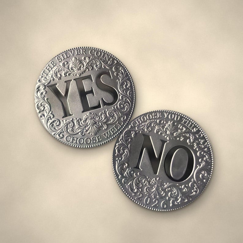 May include: Two circular silver-toned metal coins featuring ornate embossed scrollwork borders. One coin displays the word YES with the text THE SILVER COINS CHOOSE WELL. The other coin displays the word NO with the text CHOOSE YOU THIS DAY 2026.