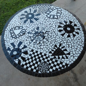 May include: A round black and white mosaic table top with a variety of geometric designs, including circles, stars, and triangles.