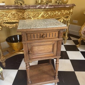 May include: A wooden bedside table featuring a rectangular green marble top, a single drawer with a small round knob, and a lower shelf. The cabinet has a door with a matching round knob, vertical fluted detailing on the sides, and four legs.