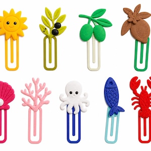 May include: A set of nine colorful paper clips featuring various decorative toppers including a yellow sun, olive branch, green olives, brown lemon, pink seashell with a pearl, pink coral, white octopus, blue fish, and a red lobster.