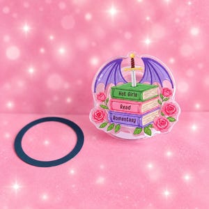 May include: An acrylic pin featuring a stack of three books with the text Hot Girls Read Romantasy, topped with a silver sword and purple dragon wings, surrounded by pink roses, accompanied by a separate dark blue circular ring component.