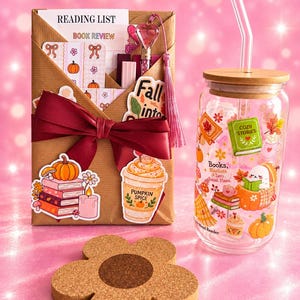 Könnte beinhalten: Ein brauner Geschenkumschlag mit dunkelroter Schleife, der eine Leseliste und Buchrezensionskarten enthält, dazu ein Glastrinkbecher mit Bambusdeckel, ein Glasstrohhalm und ein blumenförmiger Untersetzer aus Kork mit braunem Kern.