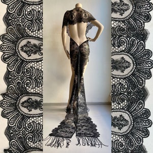 May include: A black lace shawl with a long train and fringe. The shawl is made of delicate lace with a floral pattern. The shawl is draped over a mannequin.
