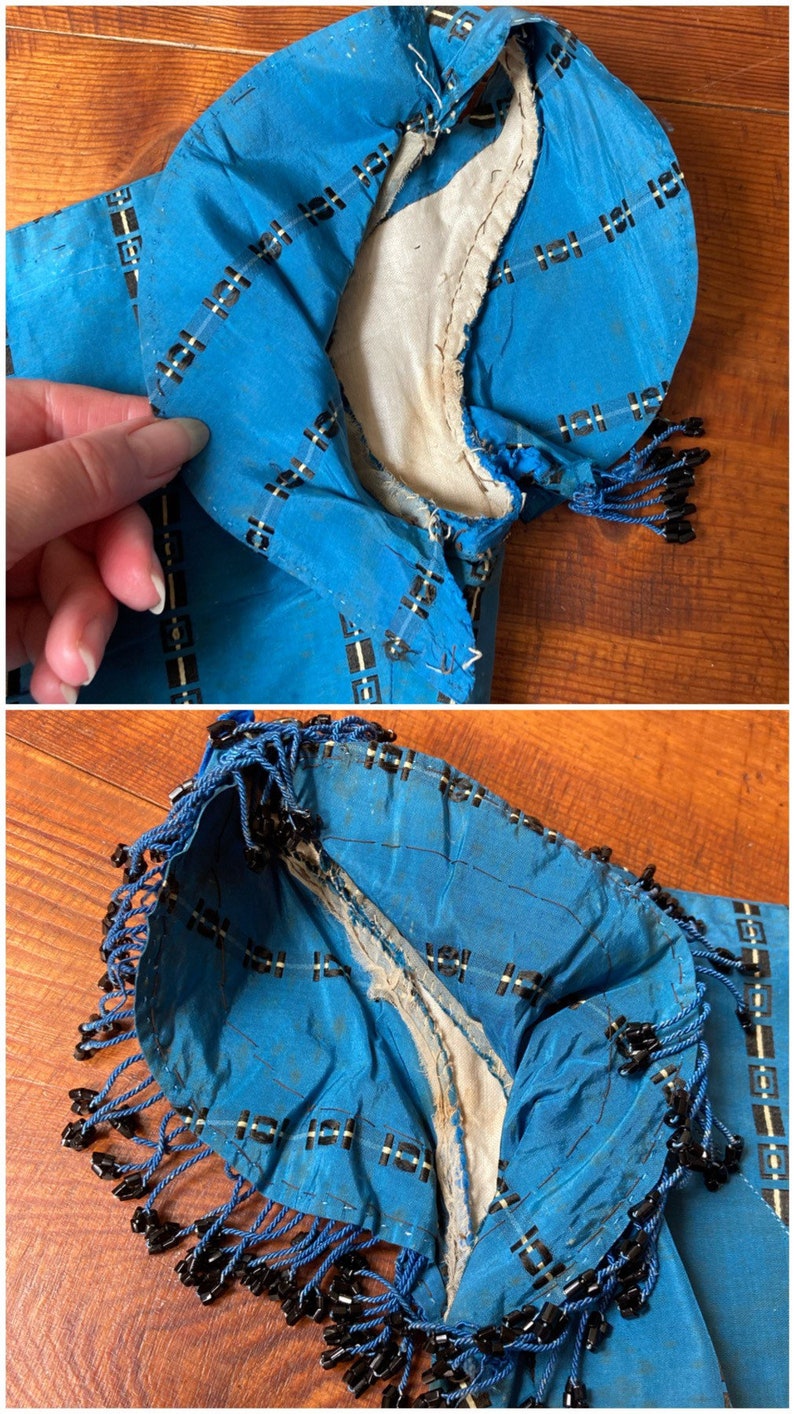 May include: A blue silk fabric with a black and white geometric pattern. The fabric has a fringe trim with black beads. The fabric is worn and has some tears.