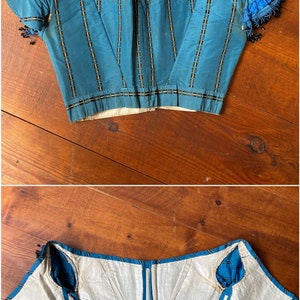 May include: A blue and white striped corset with a white lining and blue ribbon ties. The corset has a boned structure and is designed to cinch the waist.