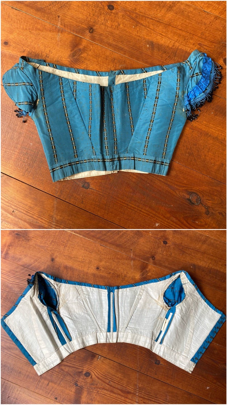May include: A blue and white striped corset with a white lining and blue ribbon ties. The corset has a boned structure and is designed to cinch the waist.