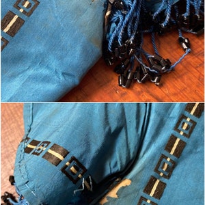May include: A close-up of a blue fabric with a black and white geometric pattern. The fabric has a frayed edge and is decorated with black beads.