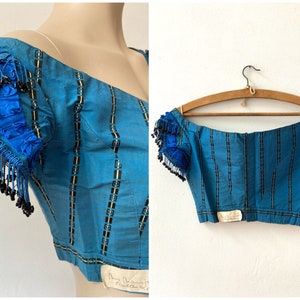 May include: A blue and black striped off-the-shoulder top with beaded trim on the sleeves. The top is made of a silky fabric and has a fitted bodice. The top is labeled "Mary Delmont Couture, Paris".