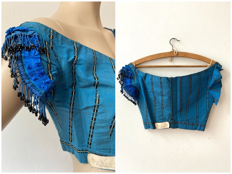 May include: A blue and black striped off-the-shoulder top with beaded trim on the sleeves. The top is made of a silky fabric and has a fitted bodice. The top is labeled "Mary Delmont Couture, Paris".