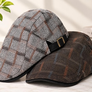May include: Two flat caps featuring a structured brim and a plaid pattern. One cap is light gray with dark gray and brown grid lines, while the other is dark brown with subtle blue and orange checkered accents. Both caps include an adjustable strap.