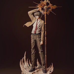May include: A standing anime-style figure of a person with brown hair, wearing a tan blazer, white shirt, red tie, and brown trousers. The figure holds a tall, ornate gold staff with a starburst top, standing on a base of sculpted skulls.