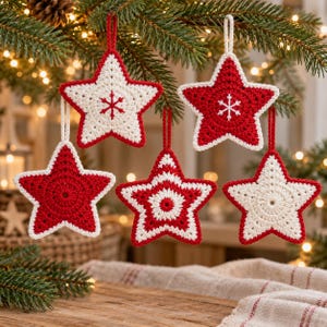 May include: Five star-shaped crochet ornaments hanging from evergreen branches. The ornaments feature red and white yarn in various patterns, including solid colors, striped designs, and embroidered snowflake motifs, each with a matching loop.