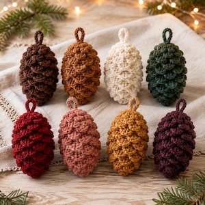 May include: A set of eight crocheted pinecone ornaments in various colors including dark brown, light brown, cream, forest green, deep red, dusty rose, mustard yellow, and plum, each featuring a small loop at the top for hanging purposes.