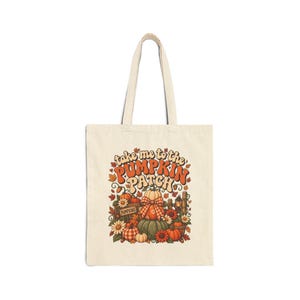 Peut inclure: Un sac fourre-tout en toile couleur crème avec une impression graphique colorée de citrouilles, de feuilles d'automne et de fleurs. Le texte "take me to the PUMPKIN PATCH" est imprimé dans une police rétro au-dessus d'une caisse en bois.