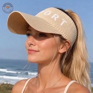 May include: A beige knit visor with a wide brim and the word SPORT embroidered in white capital letters across the front band. The visor features a textured ribbed pattern throughout the crown and brim, providing a structured yet flexible fit.
