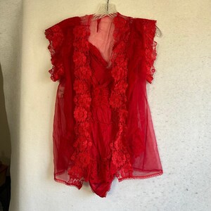 May include: A vibrant red sheer robe featuring short sleeves and a deep V-neckline. The garment is adorned with intricate floral lace trim along the front opening and sleeve edges, creating a layered texture over the semi-transparent fabric.