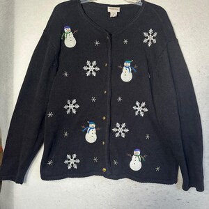 May include: A black long-sleeve button-down cardigan featuring embroidered white snowmen with colourful scarves and hats, interspersed with white snowflake patterns of varying sizes across the front of the knit garment.